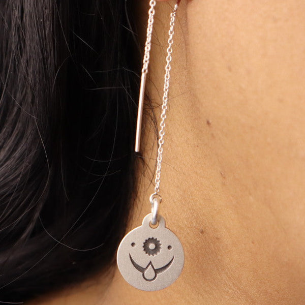 Close-up of a sterling silver threader earring with an engraved celestial face design, worn on a woman’s ear.