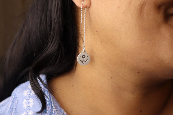 Close-up of a sterling silver threader earring with an engraved celestial face design, worn on a woman’s ear.