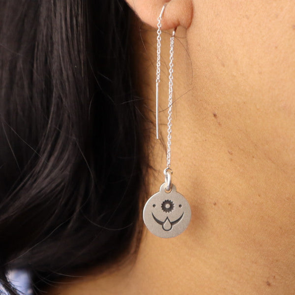 Close-up of a sterling silver threader earring with an engraved celestial face design, worn on a woman’s ear.