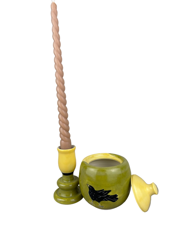 Green ceramic jar with a lid and a candle on a gray background