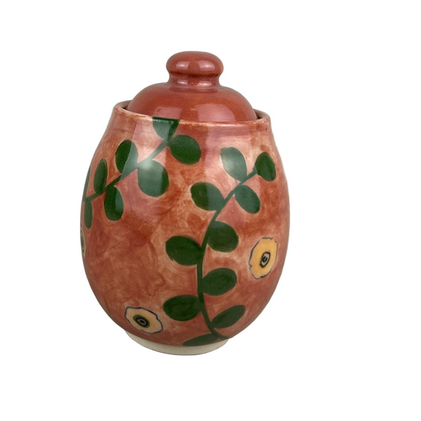 Ceramic jar with a red-brown glaze and green leaf patterns on a gray background