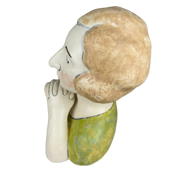 Ceramic figurine of a person with a shell on their head against a gray background