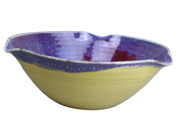 Ceramic bowl with purple interior and yellow exterior on a light gray background