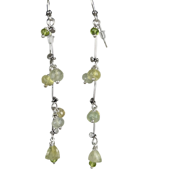 Sterling silver earrings handcrafted in a flowing vine shape with green prehnite and peridot gemstones, laid flat on a light background. Nature-inspired design with a fresh, botanical aesthetic.