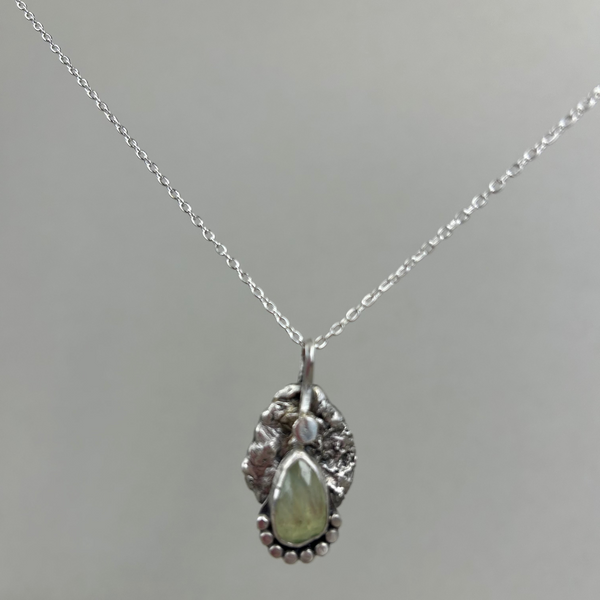 Silver necklace with a pendant featuring a green gemstone on a gray background