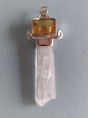 A pendant featuring a clear quartz crystal point set in rose gold with a rectangular yellow citrine gemstone at the top, shown against a plain gray background.