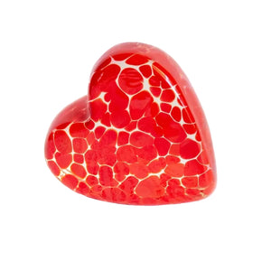 A heart-shaped red glass candle holder with a white crackle mosaic pattern, resting on an open book page against a white background.