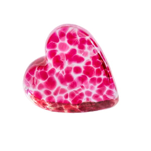 A heart-shaped glass ornament with a vibrant pink and white marbled pattern, resting on an open book page against a clean white background.