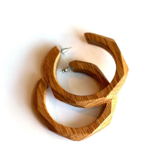 A pair of chunky, open-hoop earrings made of natural wood with a visible grain pattern, displayed on a clean white background.