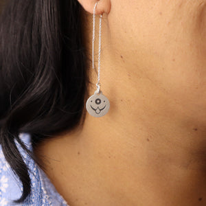 Close-up of a sterling silver threader earring with an engraved celestial face design, worn on a woman’s ear.