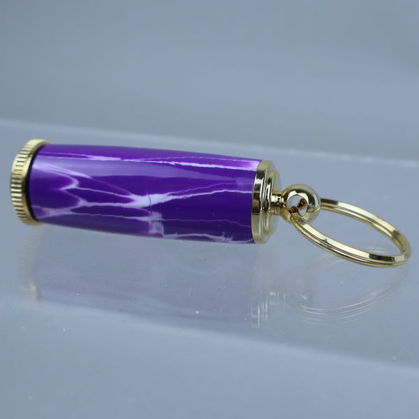 Purple cylindrical keychain with gold accents on a clear stand against a gray background