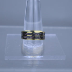 Gold ring with black stones on a clear stand against a gray background