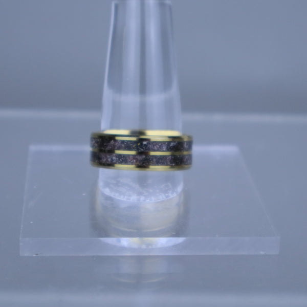 Gold ring with black stones on a clear stand against a gray background