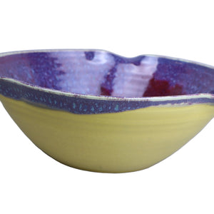 Ceramic bowl with purple interior and yellow exterior on a light gray background