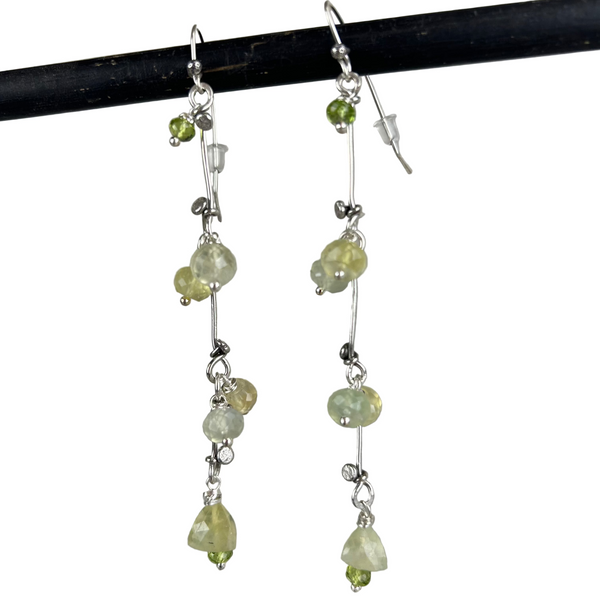 Sterling silver earrings handcrafted in a flowing vine shape with green prehnite and peridot gemstones, laid flat on a light background. Nature-inspired design with a fresh, botanical aesthetic.