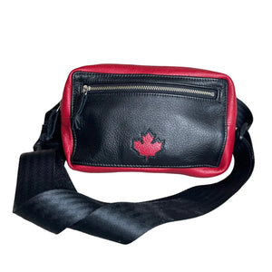 Black and red leather crossbody bag with a red maple leaf logo on the front, featuring a zippered top pocket and a wide black strap, set against a plain gray background.