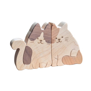 Two carved wooden cats, one with a dark brown patch and one with a light brown patch, sitting side-by-side 