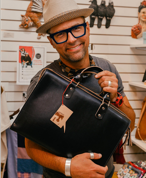 Man holding a black leather bag with a brand tag in a store setting
