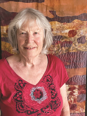 Woman wearing a red shirt with a black design in front of a colorful abstract wall hanging.
